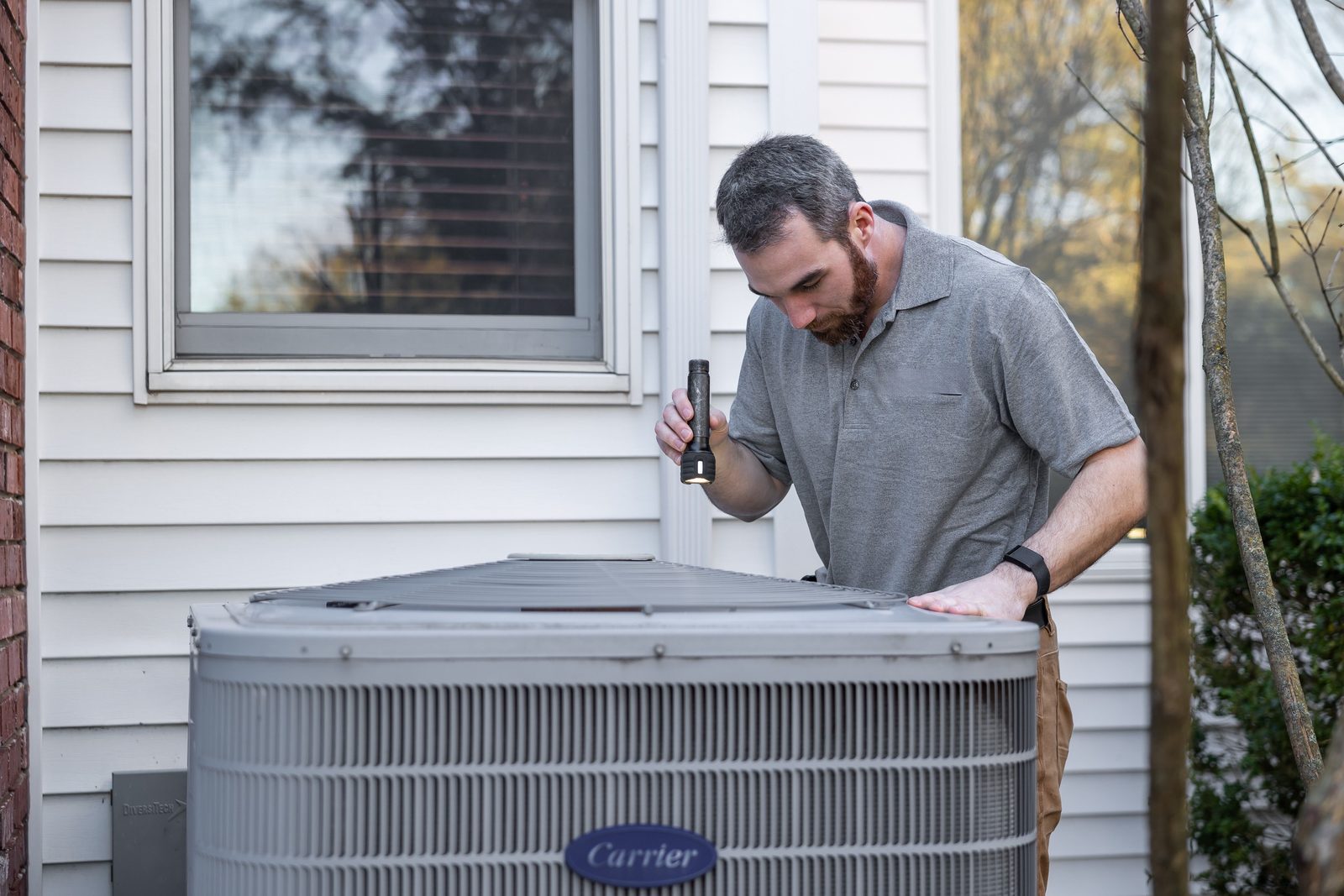 Technician inspecting an outdoor central air conditioner beside a house